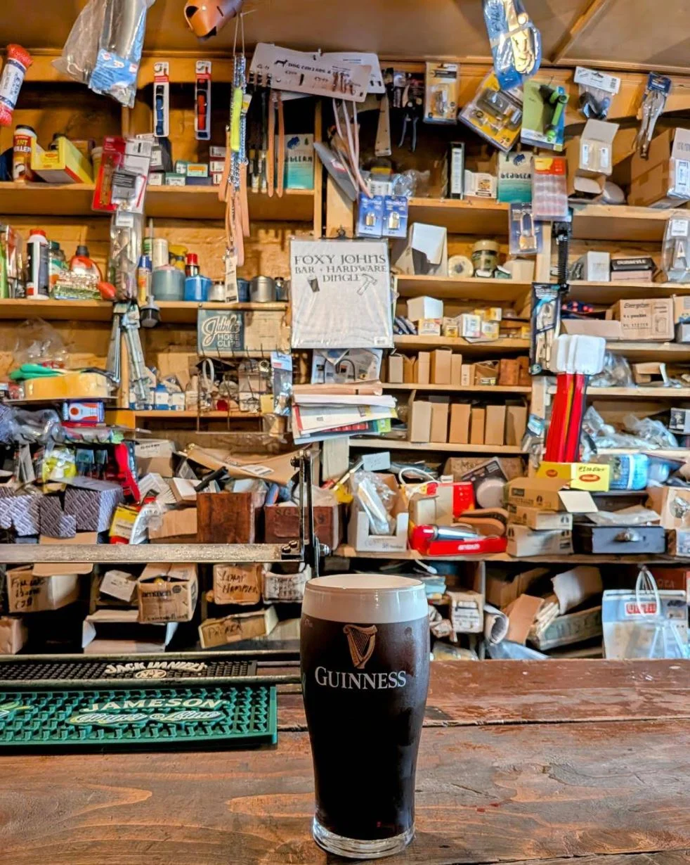 A pint of Guinness on the bar with hardware shelves and the Foxy John's sign behind